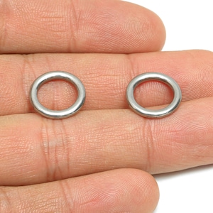 May include: Two small, silver-coloured metal rings. The rings are circular with a smooth, polished finish. They are held in a person's hand, with the rings resting on the fingers. The rings appear to be new and unused.