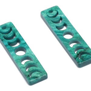 May include: Two teal green rectangular earrings with a moon phase design. Each earring has a different moon phase cut out.
