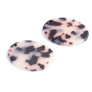 Puede incluir: Dos pendientes ovalados de resina con estampado blanco y negro con un pequeño agujero en la parte superior para colgar.