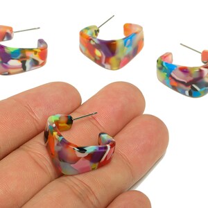 May include: A collection of colorful square hoop earrings. The earrings feature a marbled design with shades of orange, purple, blue, and green. The earrings are made of a shiny material and have a silver post.