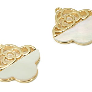 Op de afbeelding: Twee goudkleurige metalen bedels met een witte schelp inlay. Elke bedel heeft een bloemmotief.