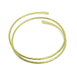 Könnte beinhalten: Zwei goldfarbene Metallarmbänder mit gehämmerter Textur. Die Armbänder sind übereinander gestapelt.