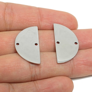Puede incluir: Dos componentes de joyería de metal plateado en forma de semicírculo. Cada pieza tiene dos pequeños agujeros para sujetar a otros componentes. Las piezas son lisas y brillantes, y probablemente se utilizan para la fabricación de joyas.