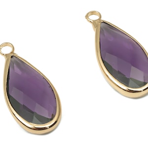 May include: Two gold-toned teardrop-shaped pendants with purple faceted glass inserts.