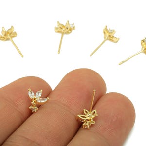 Può includere: Orecchini a bottone color oro con un design floreale. Ogni orecchino presenta un gruppo di piccole pietre chiare taglio marquise e un perno per orecchie forate. Gli orecchini sono esposti su sfondo bianco.