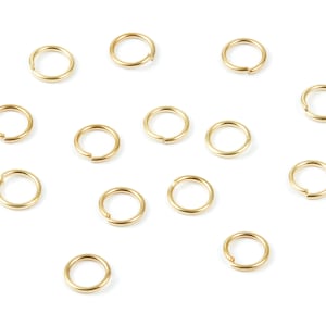 May include: A collection of 14 gold jump rings, scattered on a white background. The rings are all the same size and shape, and they are made of a shiny metal.