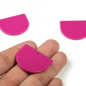 May include: Three fuchsia-colored, semi-circular acrylic charms with a small hole at the top for jewelry making. One charm is held in a hand. The charms have a smooth, glossy finish and are ideal for earrings or pendants.