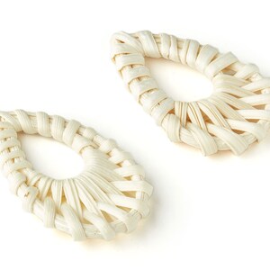 May include: Two white woven teardrop-shaped earrings. The earrings are made from a natural material and have a delicate, handcrafted look.