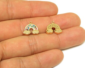 May include: Two gold-coloured rainbow charms. One charm features a rainbow design with colourful gemstones and cloud accents. The other charm is a solid gold rainbow with cloud accents. Both charms have a small loop at the top.
