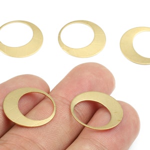Puede incluir: Cinco anillos de metal de color dorado, cada uno con una forma ligeramente curvada y abierta. Dos de los anillos se sostienen en una mano.