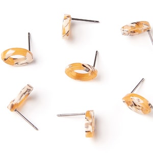 May include: Six pairs of oval-shaped earrings with a marbled pattern in shades of beige and brown. The earrings have a silver post.