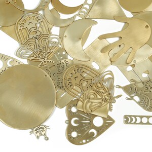May include: A collection of gold-toned metal charms featuring various shapes and designs, including butterflies, moons, hands, and hearts. Some charms have intricate cut-out patterns.