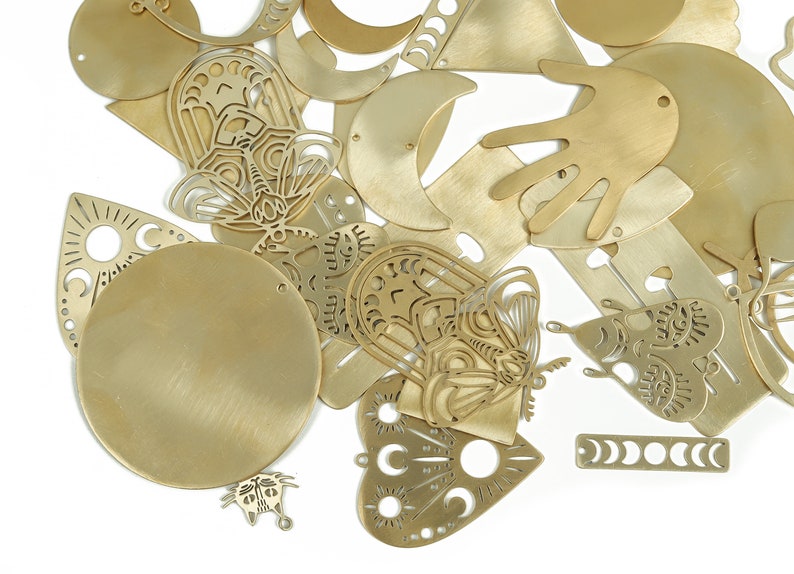 May include: A collection of gold-toned metal charms featuring various shapes and designs, including butterflies, moons, hands, and hearts. Some charms have intricate cut-out patterns.
