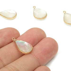 May include: Four pear-shaped pendants with a gold-colored border and a pearlescent, iridescent center. One pendant is held in a hand. The pendants have a small loop at the top for attaching to a chain or other jewelry component.