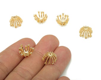 Puede incluir: Se muestran varias tapas de cuentas decorativas de color dorado sobre un fondo blanco. Las tapas de las cuentas tienen un diseño floral o de estrella, con detalles intrincados y un brillo metálico. Una tapa de cuenta se sostiene en una mano.