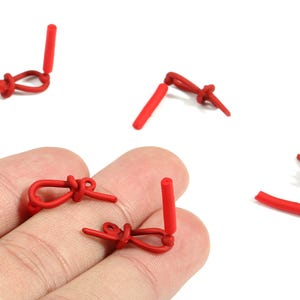 May include: Close-up of several small, bright red, knotted rubber pieces with a cylindrical post. The pieces are arranged on a light background, with some resting on a person's fingers. The objects appear to be handmade.
