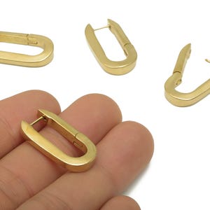 Könnte beinhalten: Goldfarbene, U-förmige Creolen. Die Ohrringe haben eine rechteckige Form mit abgerundeten Kanten und einem Klappverschluss. Das Bild zeigt mehrere Ohrringe, einige offen und einige geschlossen, vor weißem Hintergrund.