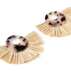 May include: A pair of earrings featuring a brown and white patterned circle with a fringe of beige raffia.