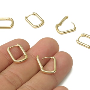 May include: Gold-colored rectangular hoop earrings. The earrings are shown in various positions, some open and some closed. The earrings are on a white background and are being held by a hand.