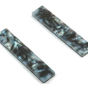 Puede incluir: Dos piezas rectangulares de joyería negras y azules con un agujero en el centro. La joyería tiene un patrón de mármol.