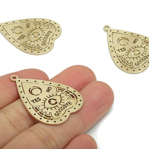 May include: Gold-colored metal Ouija board charms. Each charm is shaped like a planchette with the words "YES", "NO", and "GOODBYE" engraved. The charms have a small hole at the top for attaching to jewelry or other crafts.