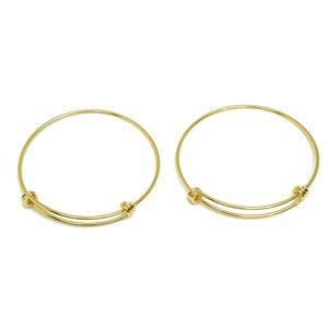 May include: Two gold-toned expandable bangle bracelets. Each bracelet has a simple, circular design with a small, round clasp.