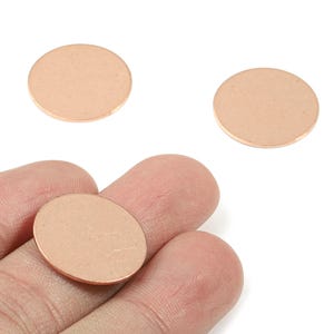 Puede incluir: Tres piezas redondas de metal de color cobre. Una se sostiene en una mano y dos están separadas. Las piezas son de un color claro y cálido y tienen un acabado liso y mate. Ideal para la fabricación de joyas o manualidades.