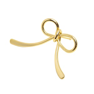 May include: A gold-colored metal bow brooch. The bow is tied in a knot and the ends of the bow are curved.