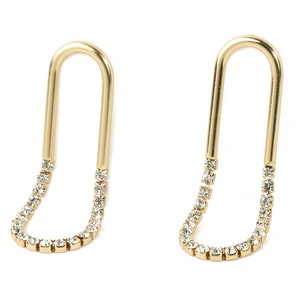 Puede incluir: Un par de pendientes de aro dorados con una fila de piedras de cristal transparentes alrededor de la parte inferior de cada aro.