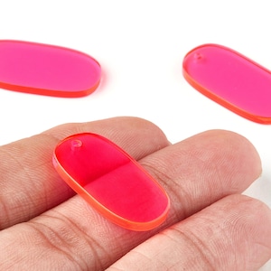 Könnte beinhalten: Drei ovale, leuchtend pinkfarbene Acrylperlen mit einem leuchtend orangefarbenen Rand. Jede Perle hat oben ein kleines Loch zum Auffädeln. Die Perlen werden vor einem weißen Hintergrund gezeigt.