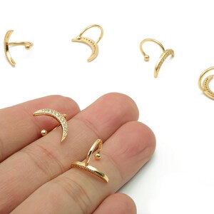 May include: Gold-toned ear cuffs in various designs, including crescent moon shapes and curved bars. Some cuffs are adorned with small, sparkling stones. The jewelry is displayed against a white background.