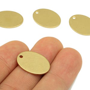 May include: Oval brass charms with a small hole for jewellery making. The charms are a warm gold colour and are shown in a close-up view. The charms are smooth and have a polished finish. These are ideal for creating necklaces, bracelets, and earrings.