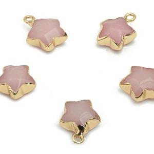 Może przedstawiać: Pięć złotych zawieszek w kształcie gwiazdy z wkładkami z różowego kamienia szlachetnego. Każda zawieszka ma pętelkę do mocowania do biżuterii.