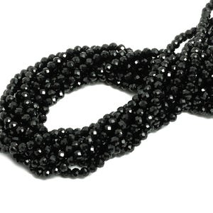 May include: A strand of black faceted gemstone beads. The beads are small and round, and they are strung together on a clear thread.