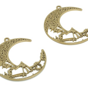May include: Two gold metal crescent moon charms with a mountain and trees design. The charms have a hole at the top for hanging.