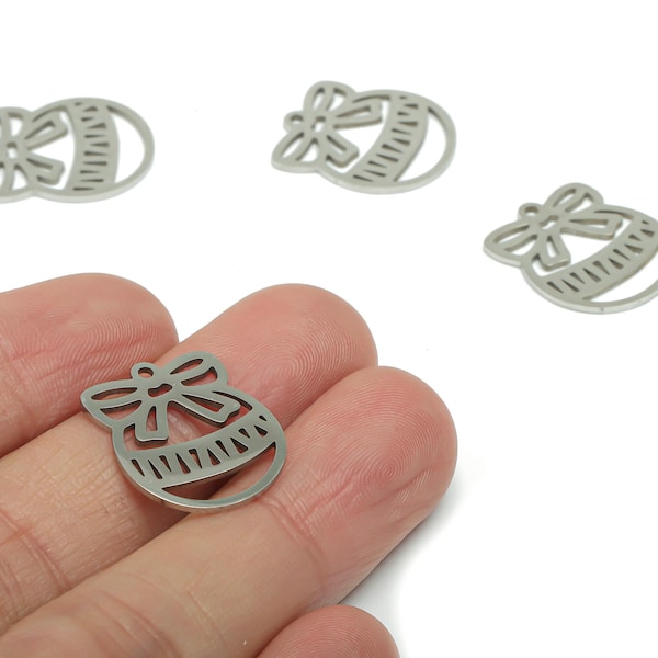 Op de afbeelding: Zilverkleurige metalen bedels in de vorm van een decoratief ornament met een strik erop. De bedels zijn uitgesneden met een gedetailleerd ontwerp en worden op een witte achtergrond getoond.