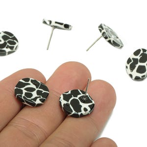 May include: Black and white stud earrings with a spotted pattern, resembling a cowhide design. The earrings are round and have a post for insertion into the ear. Several earrings are displayed.