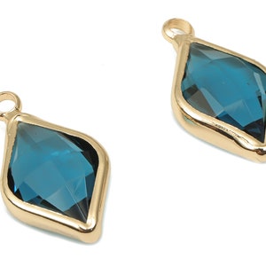 以下が含まれることがあります： 中央に青いダイヤモンド型のクリスタルをあしらった、ゴールドトーンのペンダントチャーム2個。チャームの上部には、ネックレスやブレスレットに取り付けるためのループが付いています。