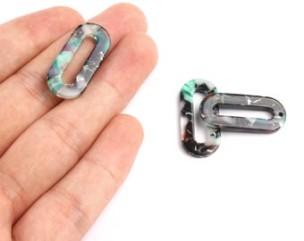 May include: Two oval-shaped acrylic beads with a marbled pattern of green, black, and white. Each bead has two holes for stringing. One bead is held in a hand, while the other is lying on a white surface.