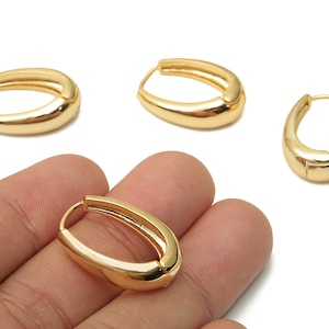 May include: Gold-colored oval hoop earrings. The earrings have a smooth, polished surface and a hinged closure. Several earrings are displayed, with one held in a hand. The earrings are a classic jewelry design.
