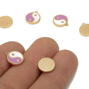 以下が含まれることがあります： 金色の金属チャーム、円形デザイン。 白とラベンダーの陰陽シンボルが付いたものと、裏面にテクスチャパターンが付いたものがあります。 これらのチャームは、ジュエリー作りに最適です。