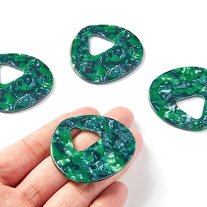 Peut inclure: Quatre pendentifs en résine marbrée verte et bleue avec une découpe triangulaire. Un pendentif est tenu dans une main. Les pendentifs ont une forme organique et une finition brillante. Ces pendentifs sont adaptés à la fabrication de bijoux.