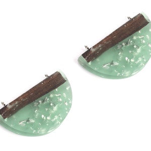 May include: A pair of green and brown resin earrings with silver flecks. The earrings are shaped like half circles and have a wooden accent.