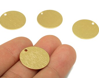 May include: Four gold-coloured, round metal charms with a brushed texture. Each charm has a small hole near the edge. One charm is held in a hand, showcasing the design. These charms are ideal for jewellery making or crafting.