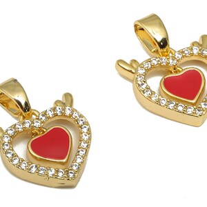 May include: Two gold heart-shaped pendants with a smaller red heart inside. The pendants are adorned with clear cubic zirconia stones.