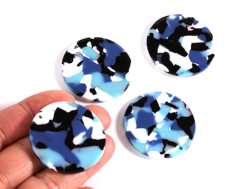 May include: Four round, flat, blue, black, and white patterned acrylic beads. The beads have a terrazzo-like design and a small hole for stringing. The beads are shown against a white background.