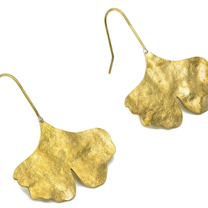 Peut inclure: Une paire de boucles d'oreilles dorées en forme de feuilles de ginkgo. Les feuilles ont une surface texturée et sont attachées à un simple crochet.