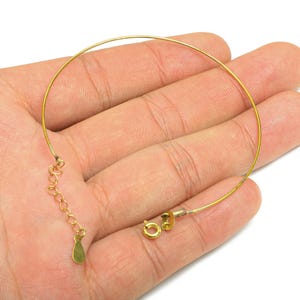 May include: A delicate gold-colored choker necklace with a thin, circular design. The necklace features a small chain and clasp for adjustable sizing. The jewelry is shown on a hand.