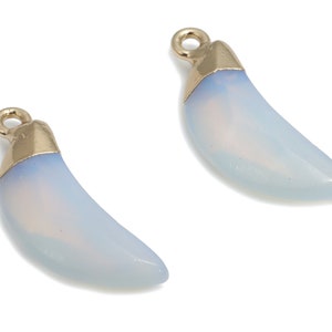 Può includere: Due ciondoli a forma di mezzaluna dorati con una finitura bianca simile all'opale. I ciondoli hanno un anello nella parte superiore per essere attaccati ai gioielli.