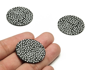 May include: Black and white round pendants with a polka dot pattern. The pendants are made of a dark material and have a hole for stringing. The image shows three pendants, one held in a hand.